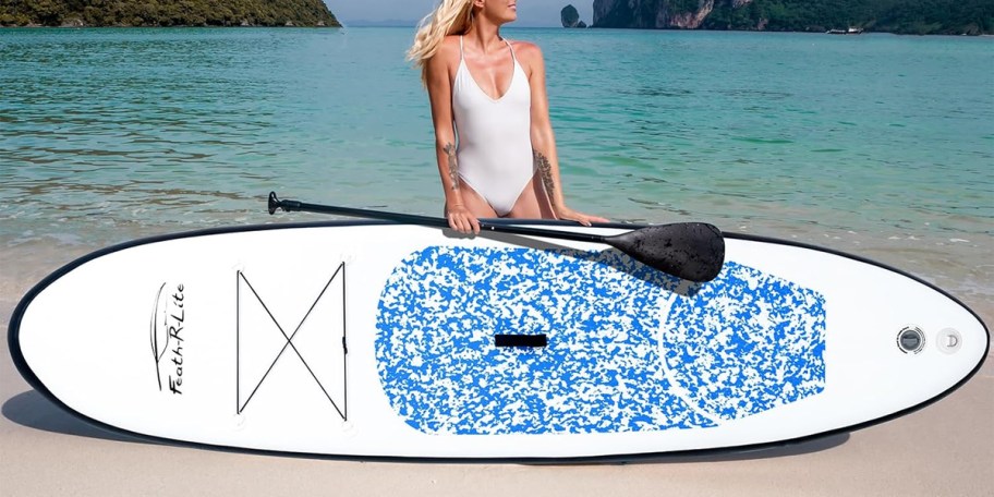 Woman holding white and blue paddleboard by the beach