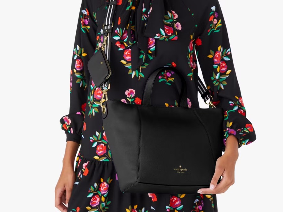 woman with a black, red, and pink floral print dress with a large black purse worn as a crossbody bag