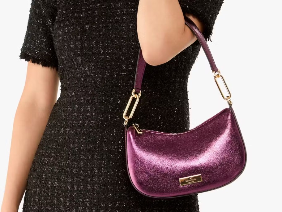 a woman wearing a black short sleeve dress and holding a purple metallic shoulder bag on her arm