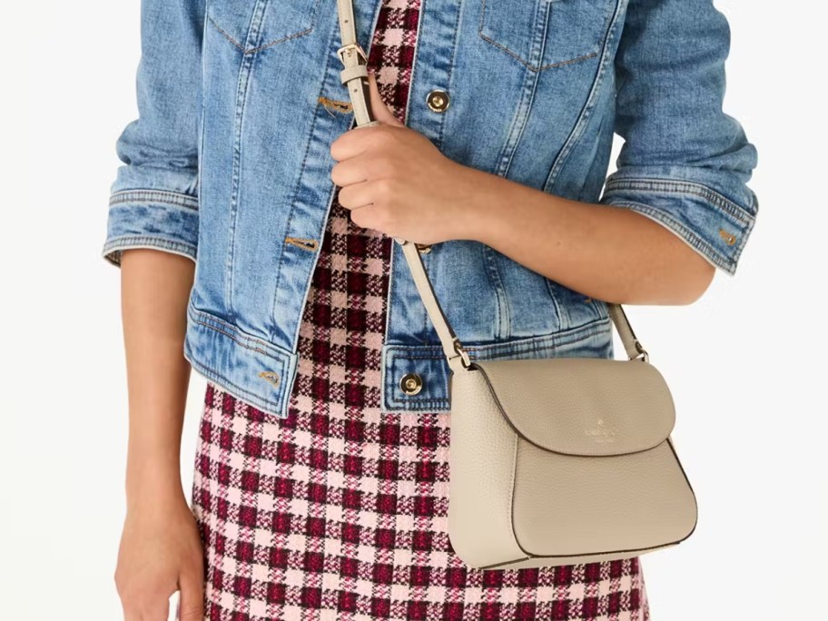 woman wearing a red and white gingham print dress and jean jacket with a light tan crossbody purse