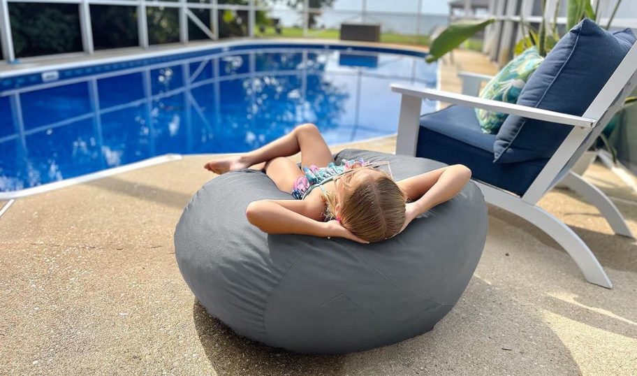 girl lounging in gray bean bag chair by pool