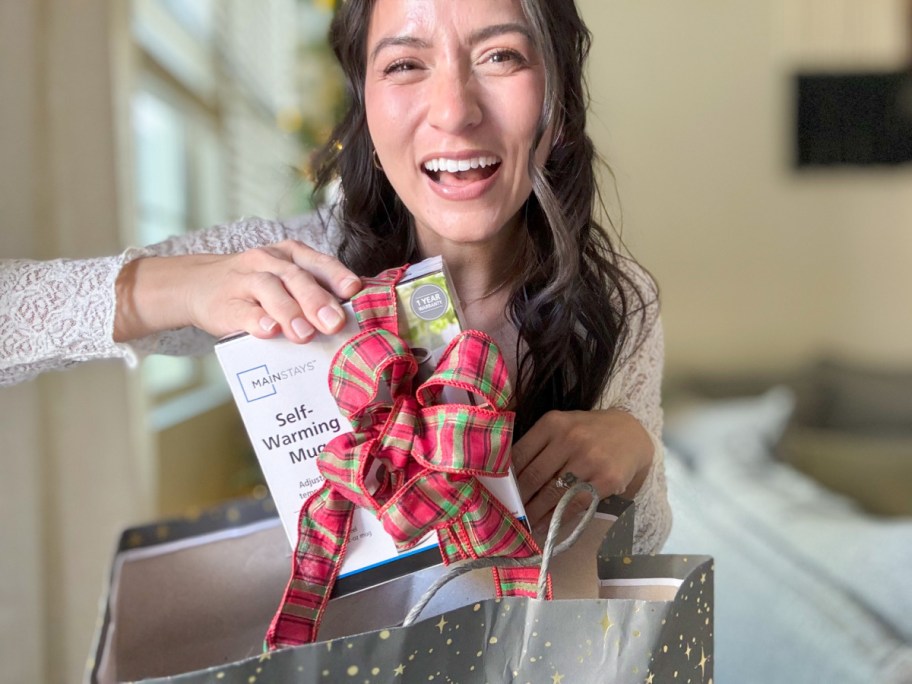 smiling woman putting a mainstays self warming mug in the box that is wrapped with a bow in a gift bag