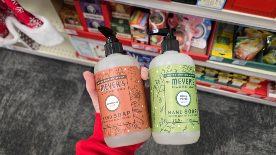 womans hand holding 2 bottles of mrs meyers hand soap