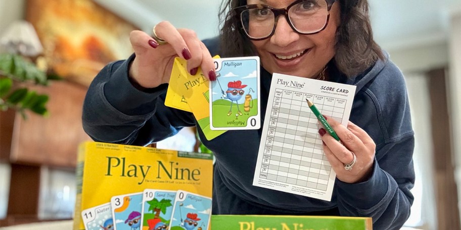 woman holding up play nine cards, pencil and scoring sheet with game box on table