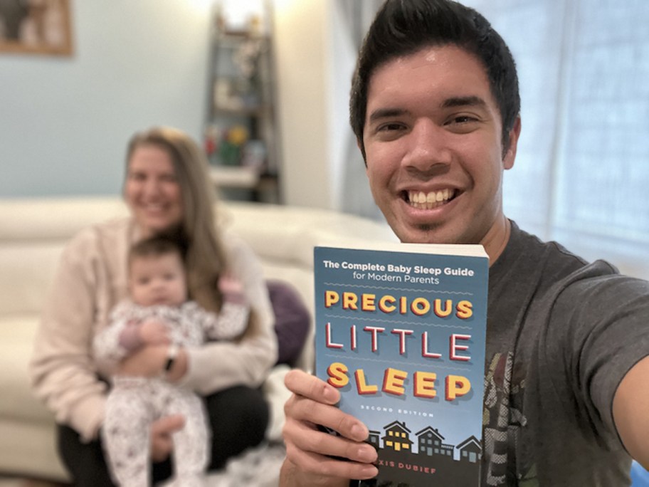 man holding a book called precious little sleep with mom and baby in background