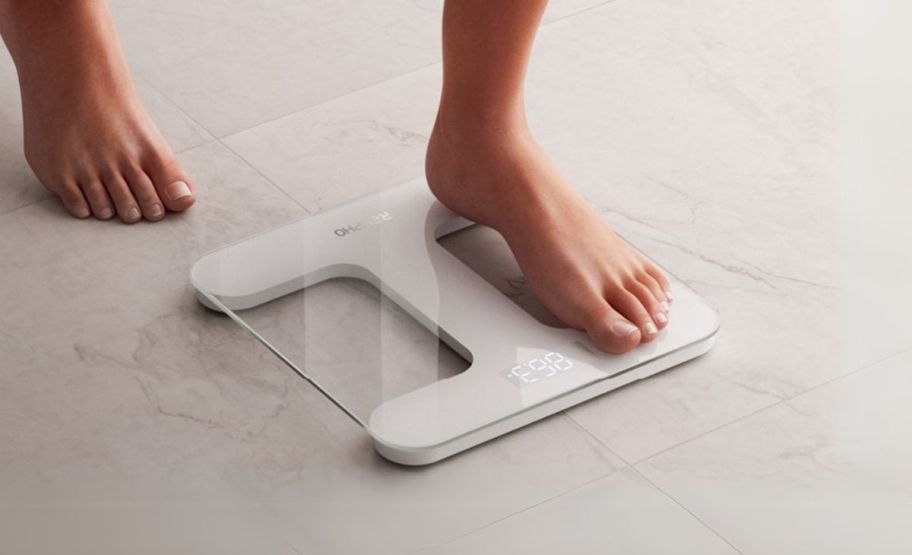 a womans feet shown stepping onto a glass bathroom scale