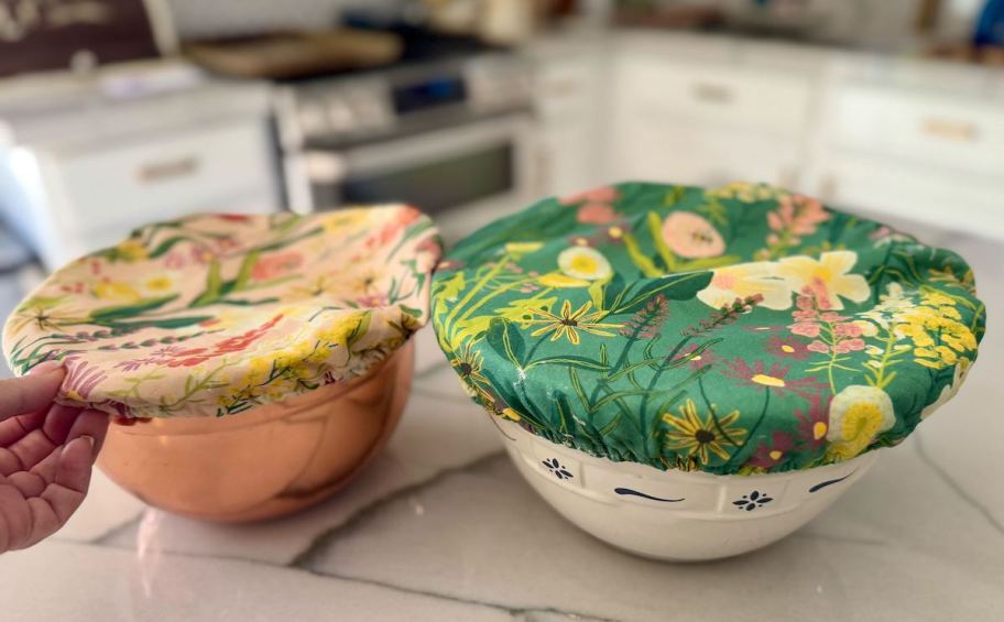 hand holding side of fabric bowl cover sitting on counter next to other bowl with cover