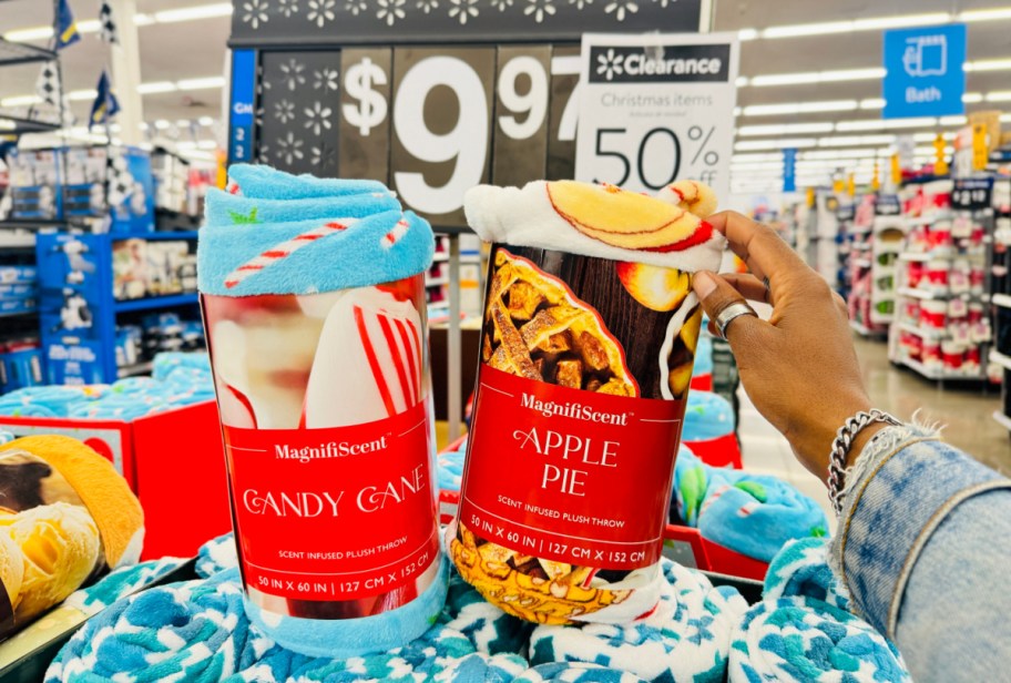 hand resting on top of two packaged scented holiday throw blankets in front of a walmart clearance sign