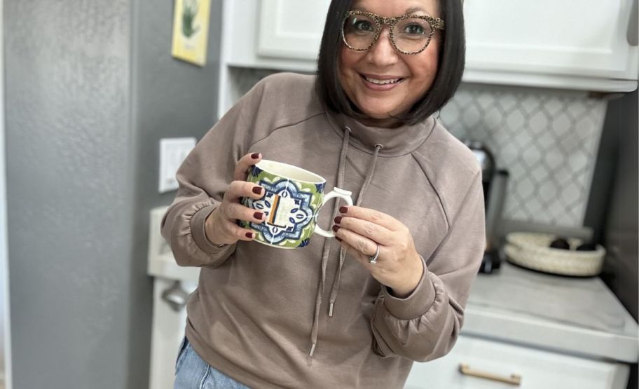 a woman in a taupe sweatshirt with a cup of tea.