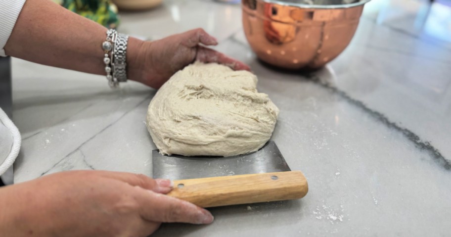 shaping a sourdough loaf with hands and dough scraper 