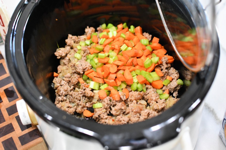 slow cooker with chopped veggies and sausage inside