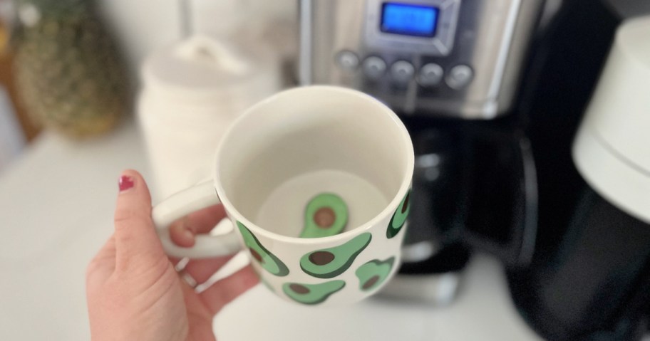 woman holding a target avocado mug in front of a coffee machine