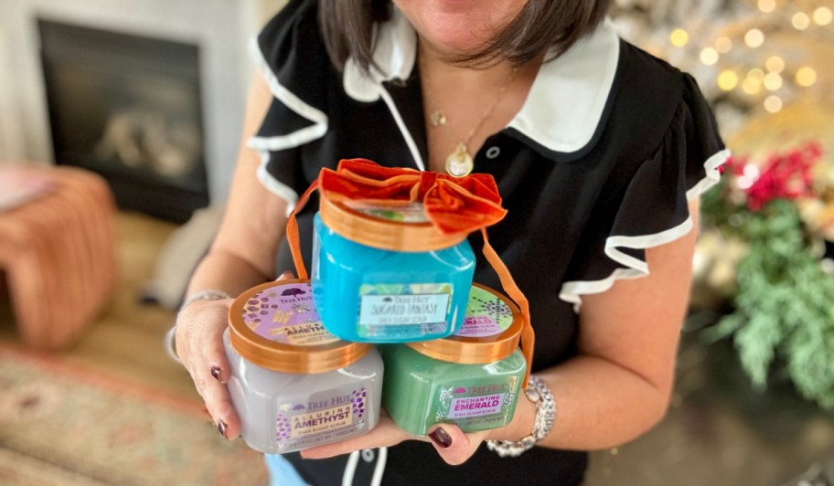 woman holding three tree hut body scrub jars with a bow on top