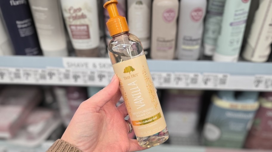 a womans hand holding a bottle of tree hut vanilla shave oil