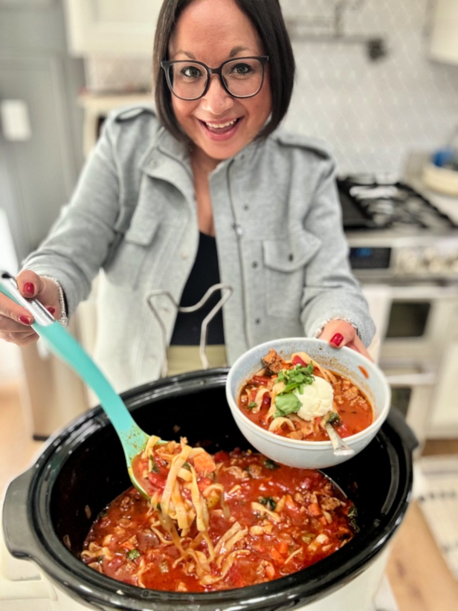 woman dishing up italian sausage soup from a slow cooker