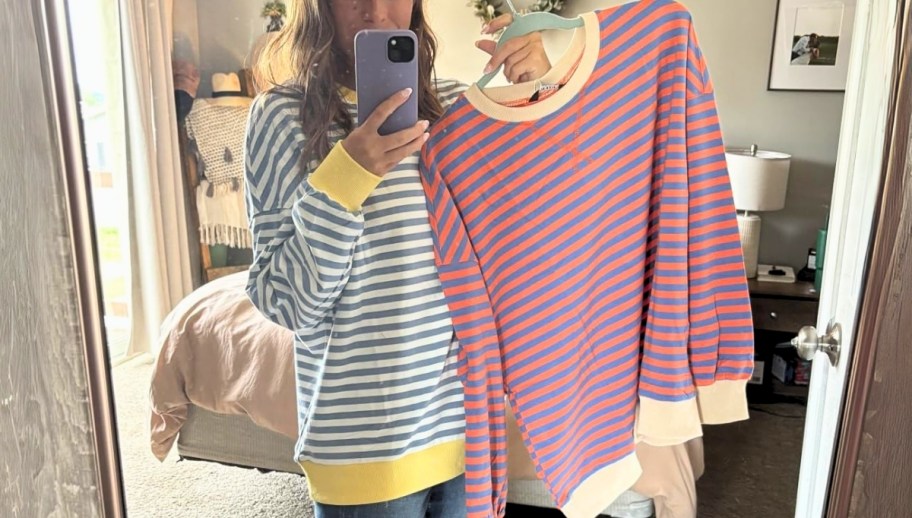 a woman taking a selfie wearing a striped sweatshirt and holding a hanger with a striped sweatshirt on it.