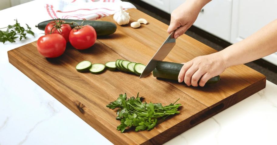 A person chopping a cucumber on a large cutting board