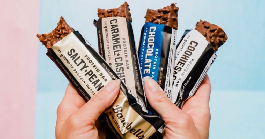 Four different barbells protein bars being held up in the sky