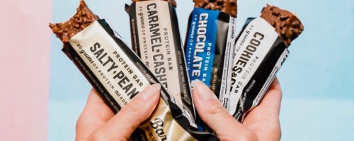 Four different barbells protein bars being held up in the sky