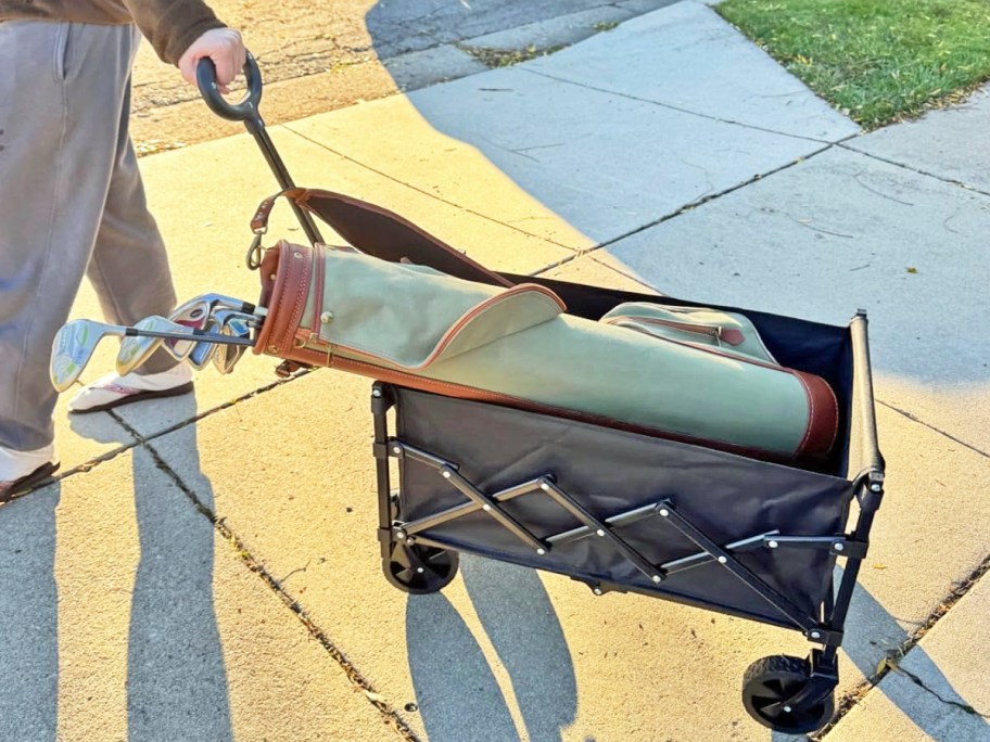 person carrying bag of golf clubs in a black wagon