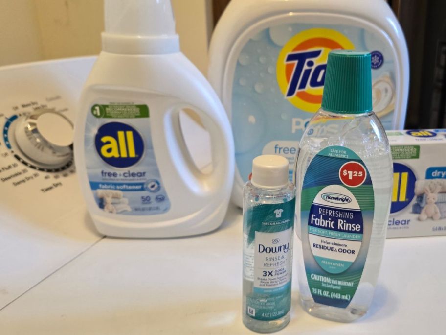 A washing machine with laundry products on it including Dollar General Laundry Rinse and Downy Rinse & Refresh