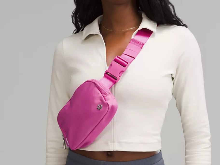 woman wearing a white long sleeve top and tan pants with a pink lululemon belt bag worn like a crossbody bag