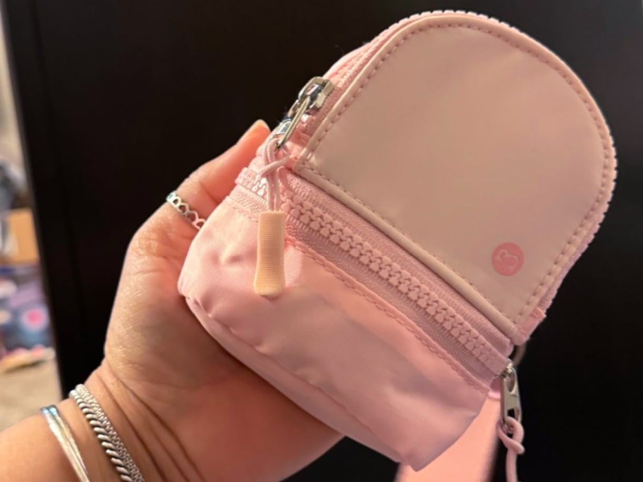 A person holding a small pink mini backpack keychain wristlet with a front zipper pocket.