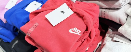 hand touching a bright pink folded nike hoodie in store