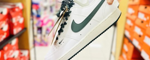 hand holding up a pair of white and green nike sneakers in store