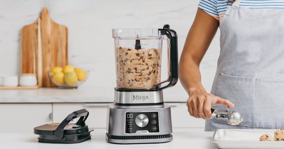 A woman scooping cookie dough out of a Ninja blender