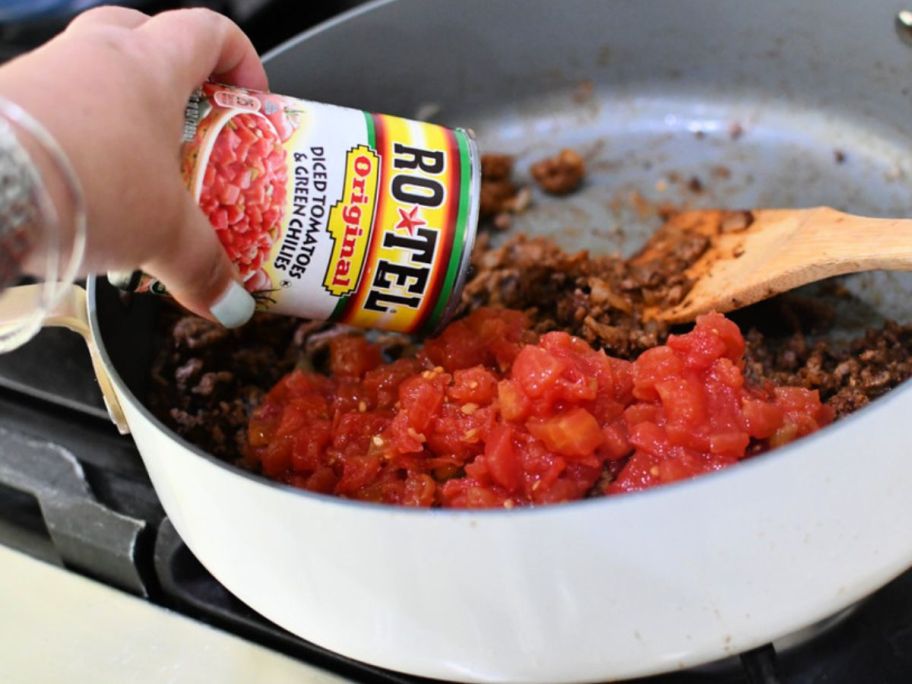 Can of Rotel being poured into a pan of browned ground beef