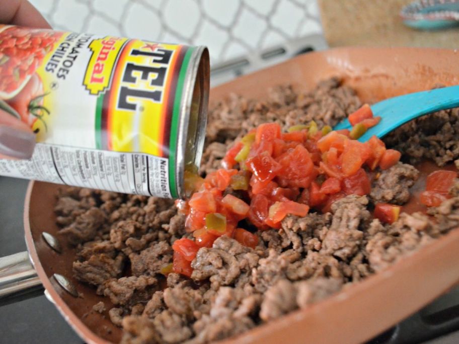 Can of Rotel being poured into a pan of cooked ground beef