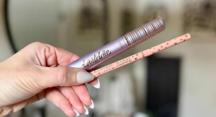 hand holding a tarte mascara and a highlighting eye pencil