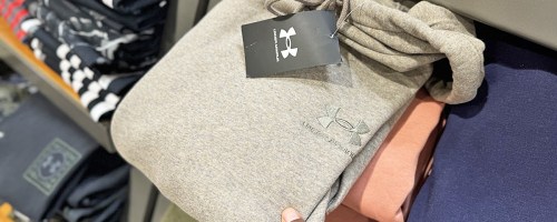 hand grabbing a folded under armour hoodie from store shelf