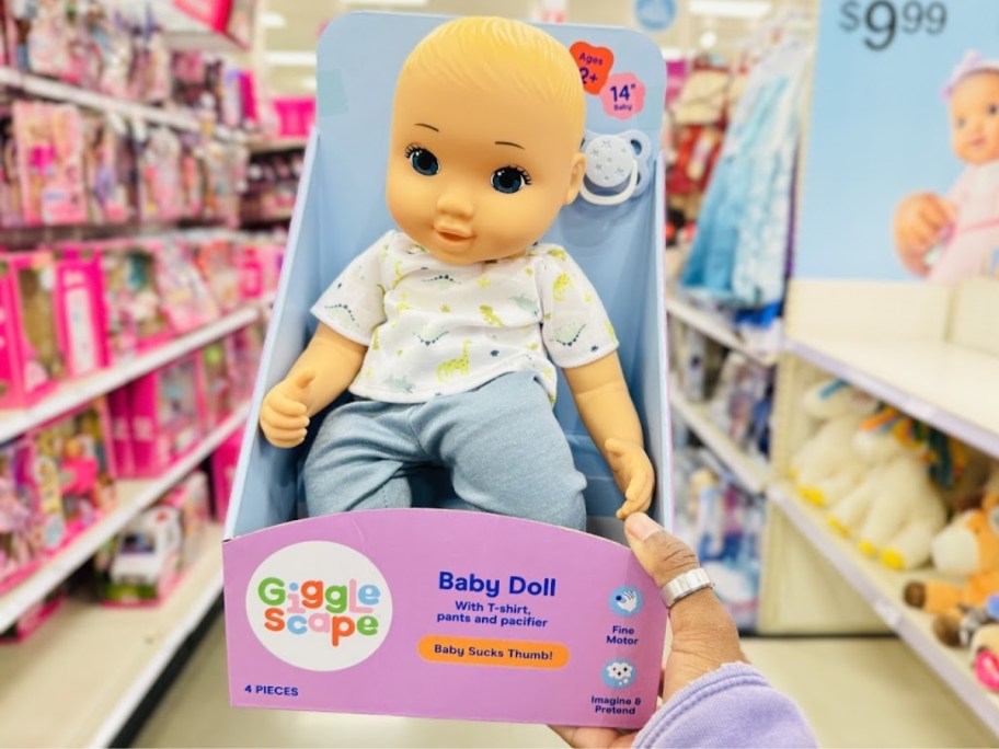 hand holding a box with a baby boy doll with blue eyes and blond hair wearing a blue and white outfit