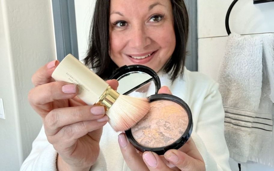 a woman holding a foundation brush to a pan of baked foundation