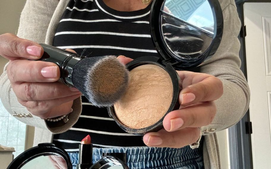 a womans hand holding a foundation brush to a pan of baked foundation