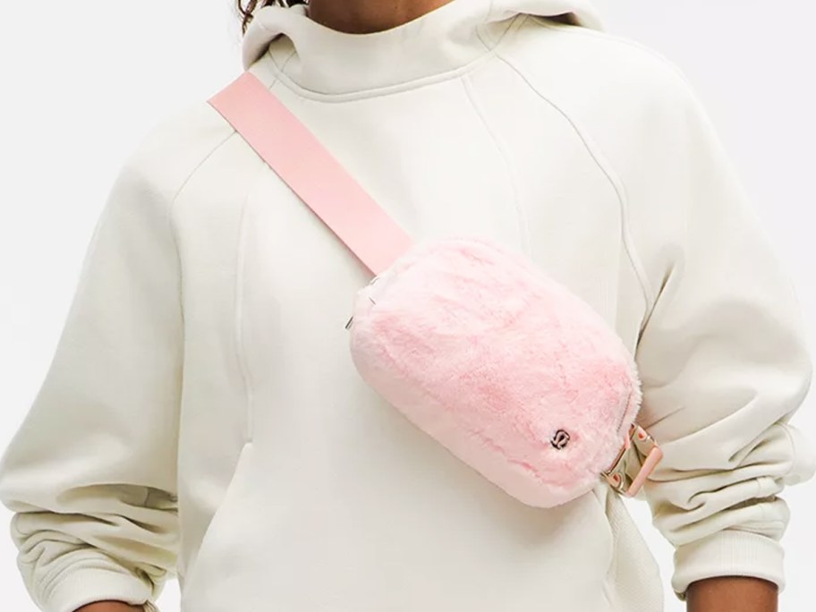 woman in a white hoodie with a plush pink belt bag across chest 