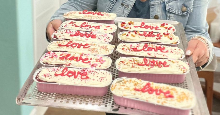 woman holding tray of mini loaf pans with "love" written on the cakes