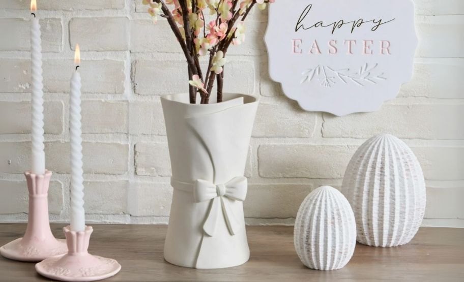 a white ceramic vase shown with candles on a tabletop