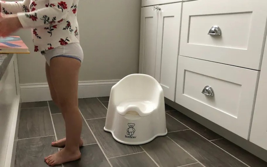 toddler standing in bathroom next to potty training toilet