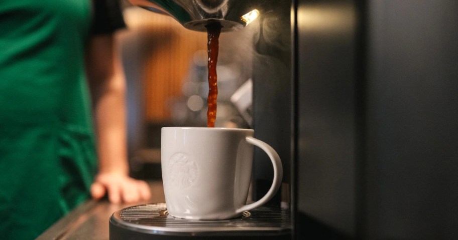 Starbucks barista in a green apron pouring coffee from a coffee machine into a white mug