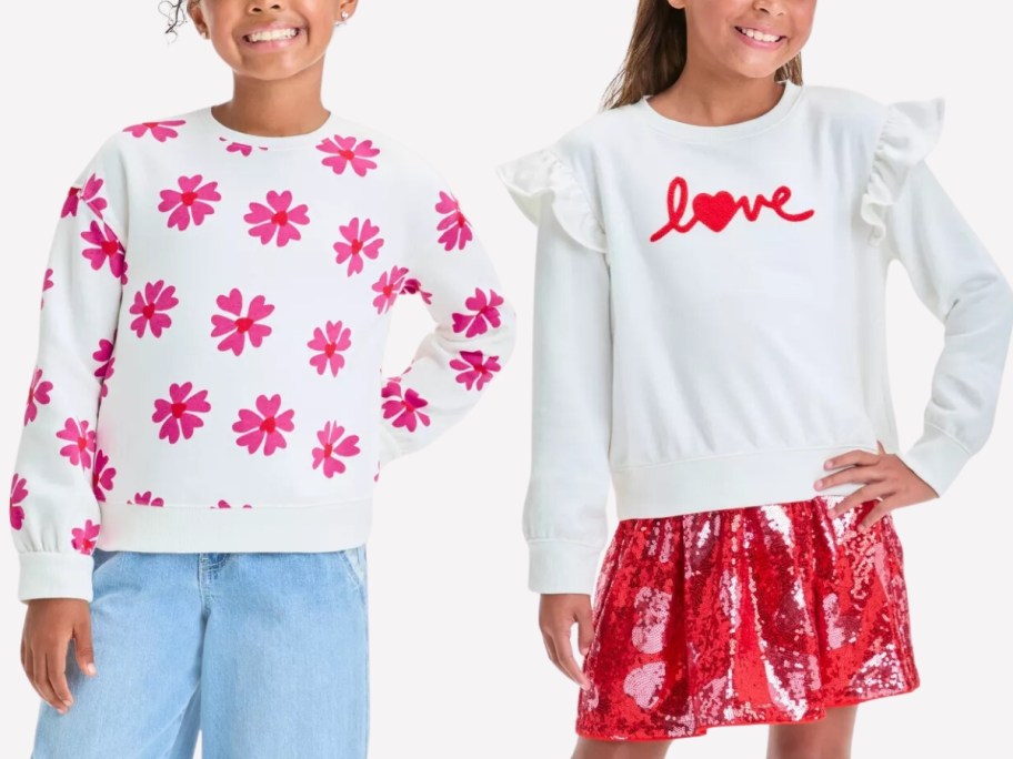 a girl wearing a white sweatshirt with pink flowers and hearts and jeans, and a girl wearing a white sweatshirt with ruffle sleeves and the word "love" with a red shimmery skirt