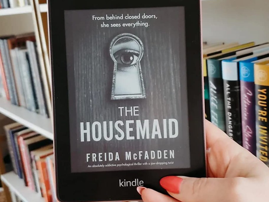holding a Kindle showing the cover of The Housemaid book