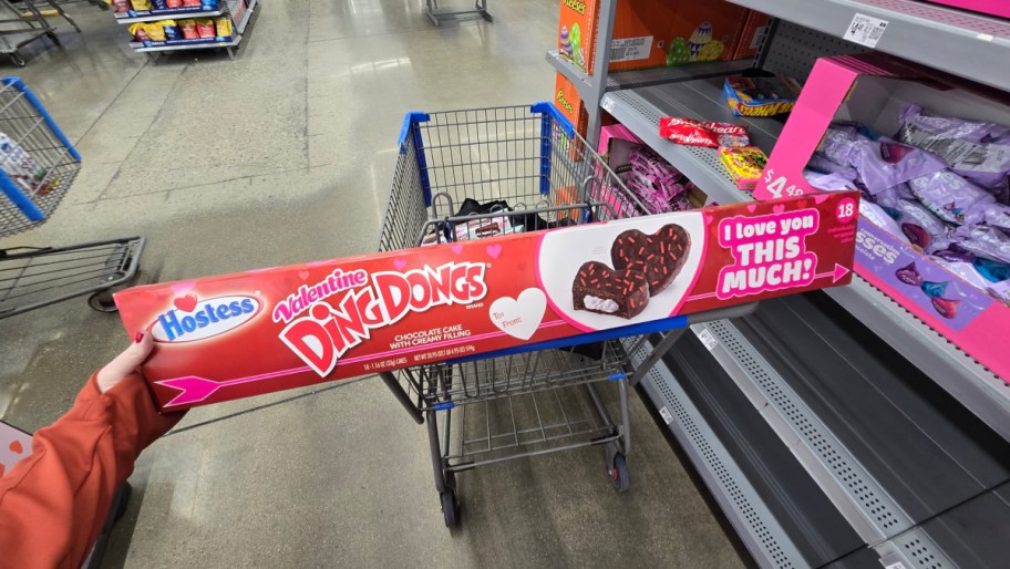 hand holding a huge box of heart shaped valentines ding dongs that is resting on a walmart shopping cart in the aisle