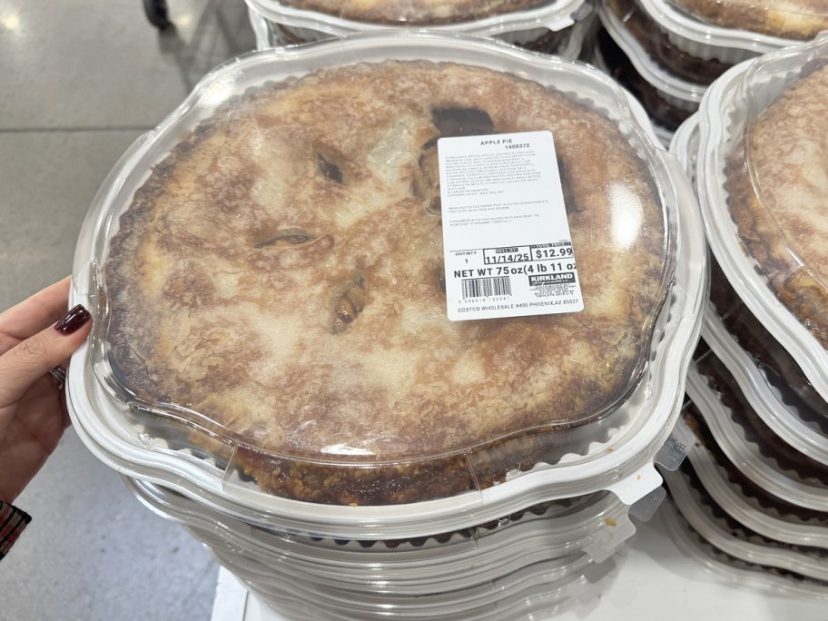 hand touching a stack of large apple pies on store table