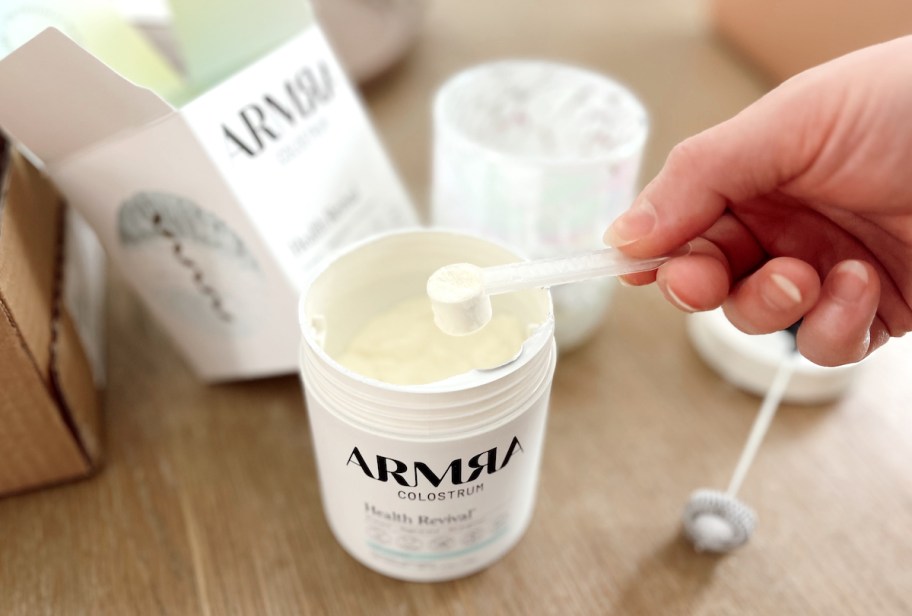 hand scooping Armra colostrum powder from jug on table
