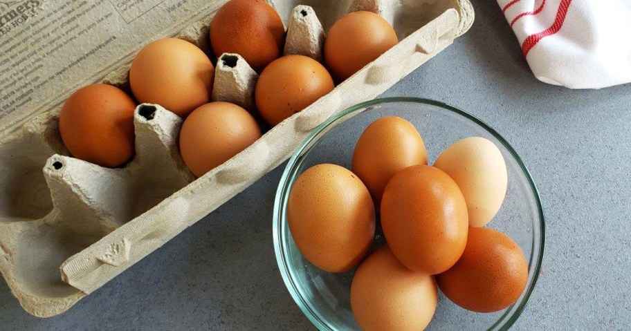 dozen brown eggs in carton and glass bowl