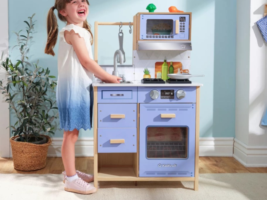 a little girl playing on a wooden play kitchen set