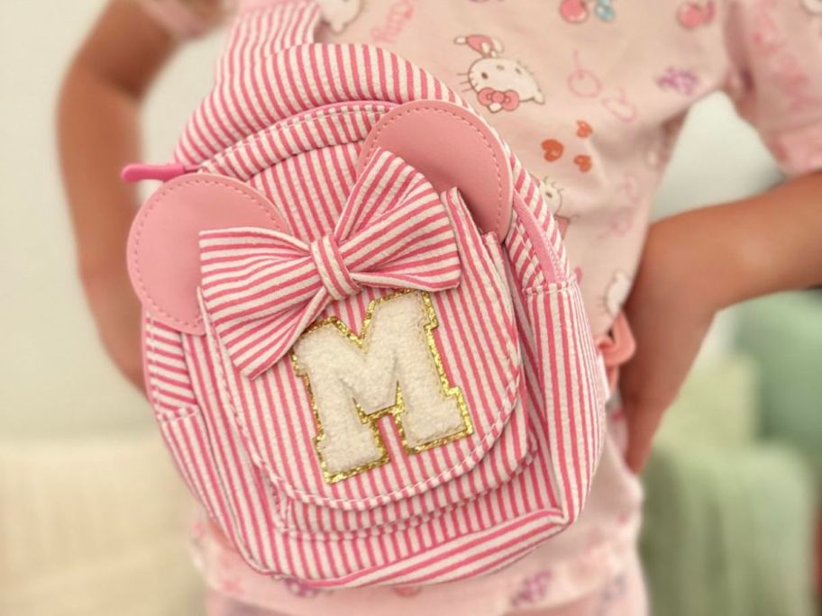 girl wearing a white and pink striped crossbody bag with the letter "M" on it